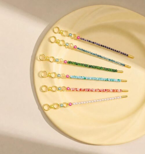 Assorted wholesale beaded joint holder sticks featuring gold rings, colorful crystal beads, and pearls on a ceramic plate