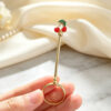 Gold joint holder ring topped with cute red enamel cherries held on a finger
