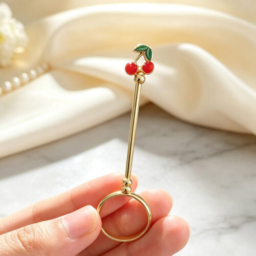 Gold joint holder ring topped with cute red enamel cherries held on a finger